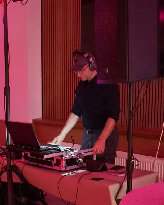 DJ Garvin mit Kopfhörern am Pult, umgeben von Lautsprechern und Lichttechnik
